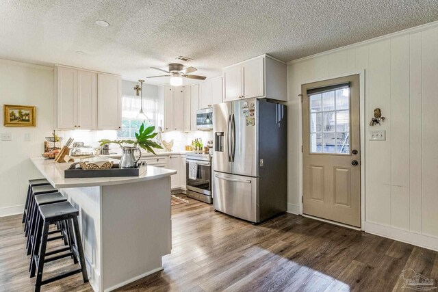 kitchen featuring pendant lighting, kitchen peninsula, sink, appliances with stainless steel finishes, and white cabinetry