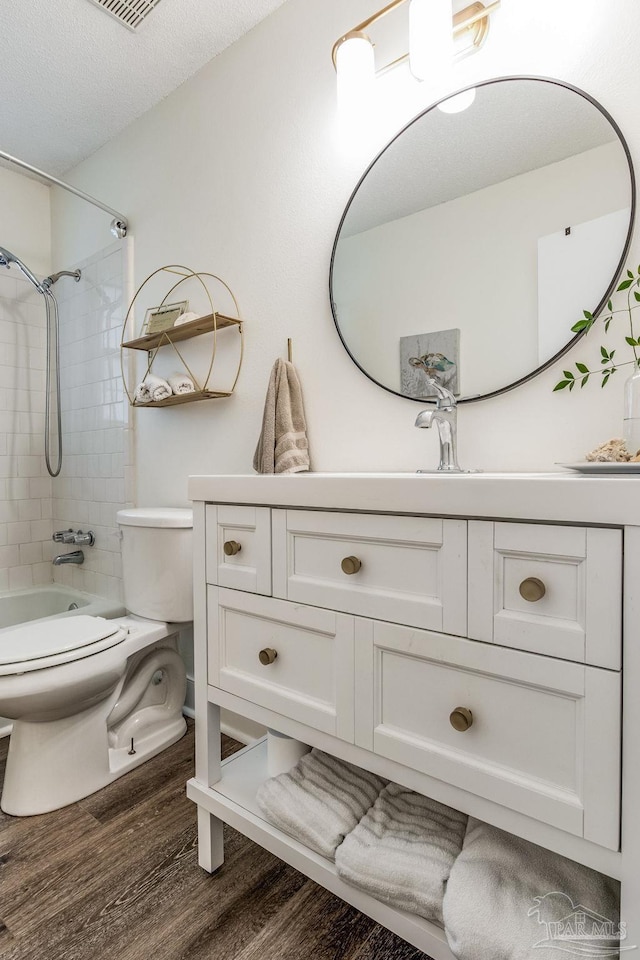 full bathroom featuring vanity, tiled shower / bath combo, a textured ceiling, wood-type flooring, and toilet