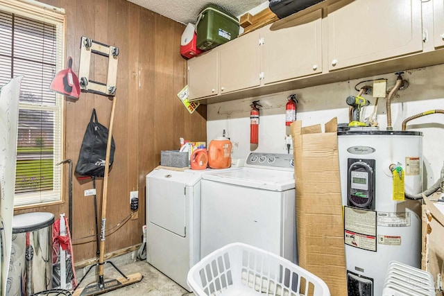 washroom with electric water heater, washer and dryer, cabinets, and wood walls