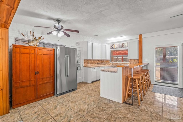 kitchen with high end fridge, a breakfast bar area, kitchen peninsula, white cabinets, and a textured ceiling