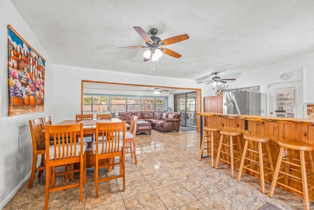 dining room with a textured ceiling, indoor bar, and ceiling fan