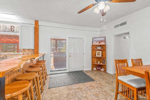 dining room with lofted ceiling, wet bar, light tile patterned floors, a textured ceiling, and ceiling fan