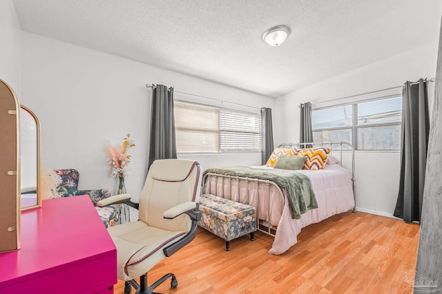 bedroom with multiple windows, a textured ceiling, and light hardwood / wood-style flooring