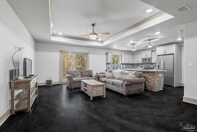 living room with a raised ceiling, ceiling fan, and a textured ceiling