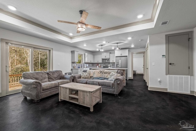 living room featuring a raised ceiling, sink, a textured ceiling, and ceiling fan