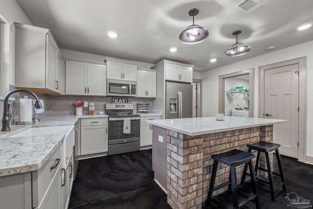 kitchen featuring pendant lighting, white cabinetry, stainless steel appliances, a center island, and light stone countertops