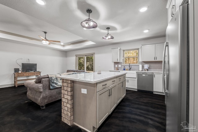 kitchen featuring light stone counters, a center island, appliances with stainless steel finishes, a tray ceiling, and pendant lighting