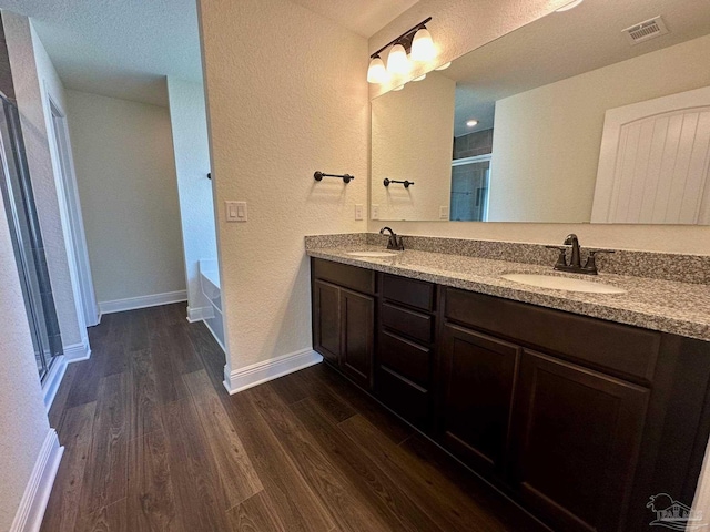 full bath featuring a sink, a textured wall, wood finished floors, and visible vents