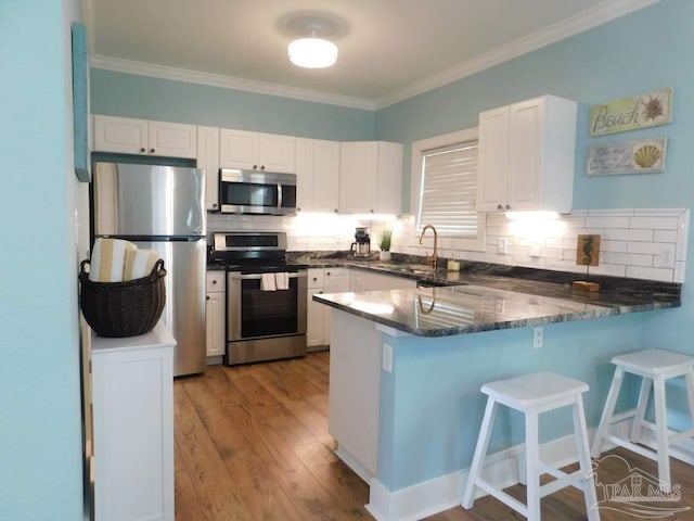 kitchen with tasteful backsplash, white cabinets, appliances with stainless steel finishes, a peninsula, and a sink