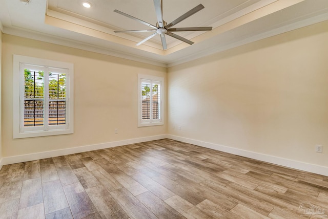 empty room with ornamental molding, light wood-type flooring, a raised ceiling, and a healthy amount of sunlight