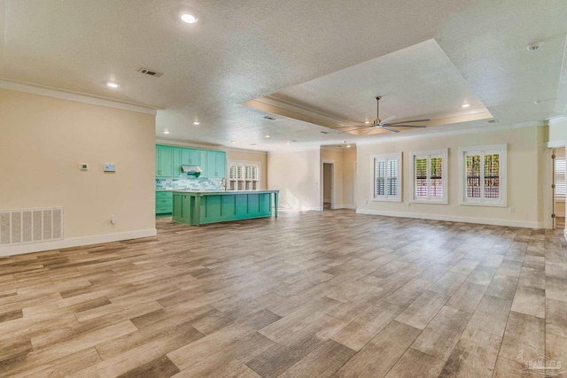 unfurnished living room with ceiling fan, light hardwood / wood-style floors, a textured ceiling, and a tray ceiling