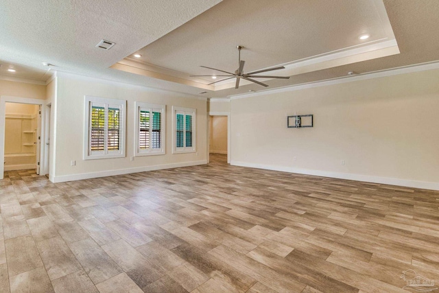 empty room with ornamental molding, a textured ceiling, a raised ceiling, ceiling fan, and light hardwood / wood-style floors