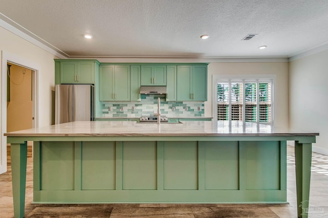 kitchen featuring light stone counters, a large island with sink, and stainless steel refrigerator