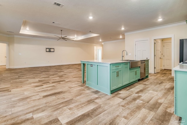 kitchen with ceiling fan, sink, light hardwood / wood-style flooring, an island with sink, and a tray ceiling