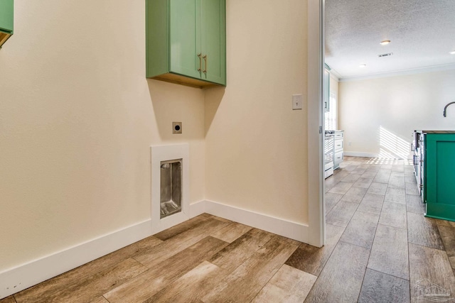 laundry area with cabinets, electric dryer hookup, light hardwood / wood-style flooring, crown molding, and a textured ceiling