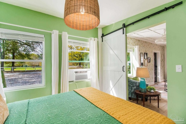 bedroom featuring multiple windows, cooling unit, wood-type flooring, and a barn door