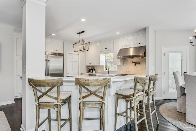 kitchen with built in fridge, dark hardwood / wood-style flooring, backsplash, a breakfast bar area, and white cabinets