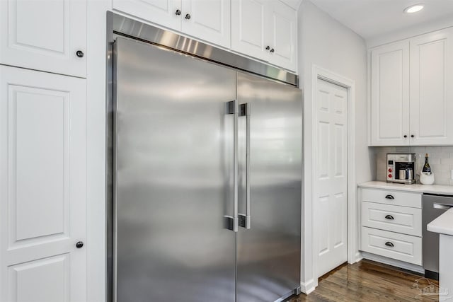 kitchen with white cabinets, decorative backsplash, built in refrigerator, and dark wood-type flooring