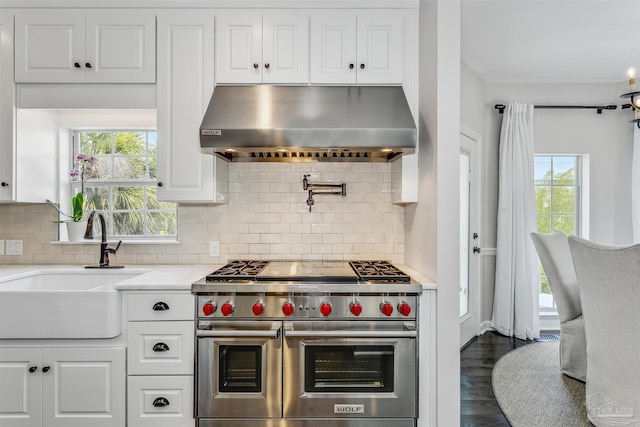 kitchen with backsplash, range with two ovens, sink, wall chimney exhaust hood, and white cabinetry