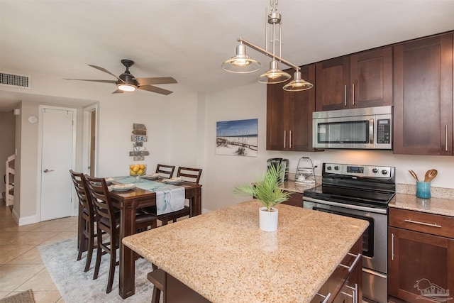 kitchen featuring pendant lighting, light stone countertops, light tile patterned floors, appliances with stainless steel finishes, and a kitchen island