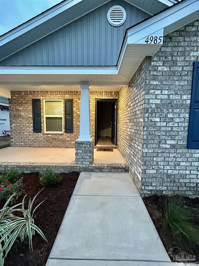 view of exterior entry with a porch and brick siding