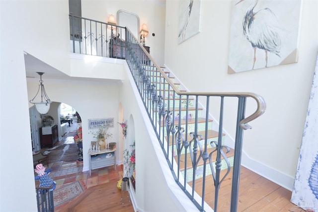 stairway featuring a towering ceiling, baseboards, arched walkways, and wood finished floors