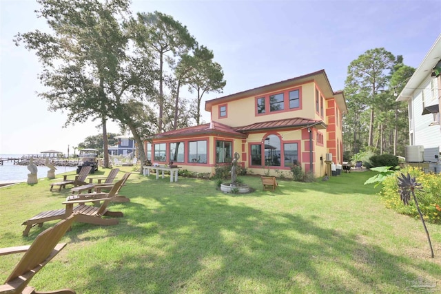 back of house featuring a water view, a lawn, a standing seam roof, metal roof, and cooling unit