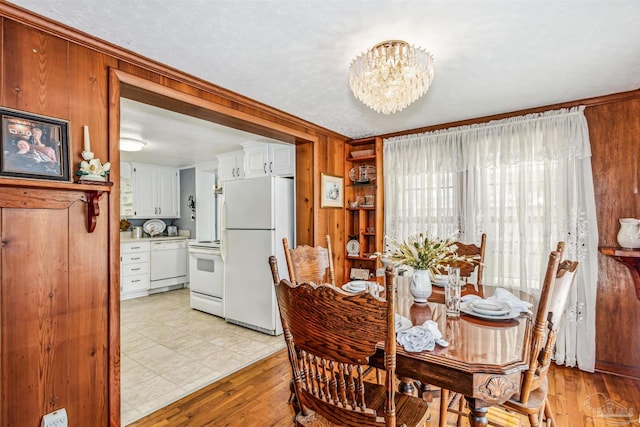 dining room featuring light wood-type flooring, an inviting chandelier, crown molding, and wood walls