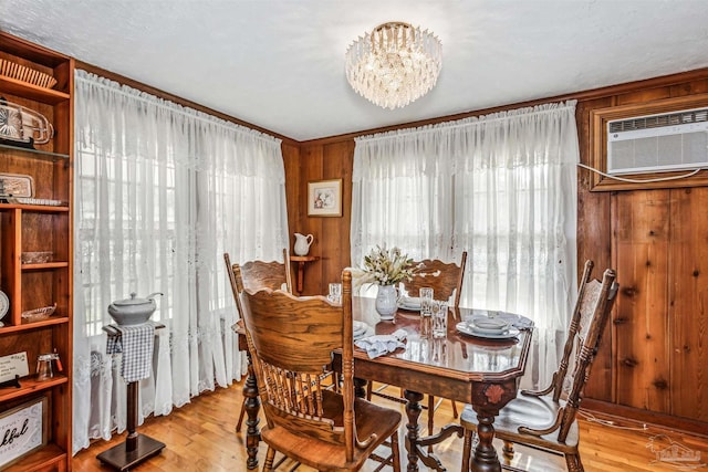 dining space with wood walls, a notable chandelier, light hardwood / wood-style floors, and an AC wall unit