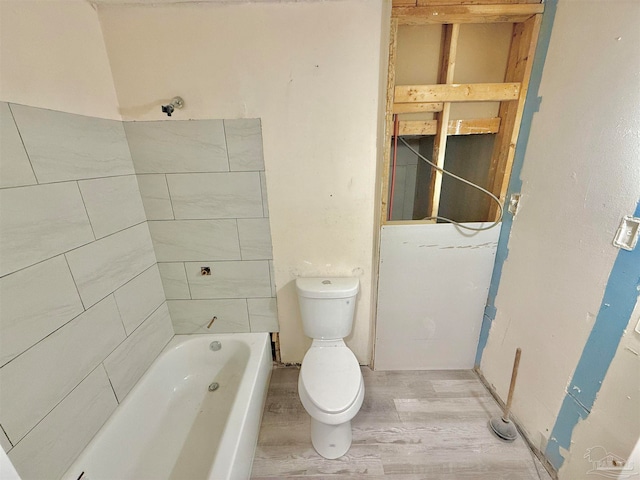 bathroom with wood-type flooring, a tub to relax in, and toilet