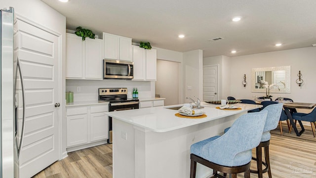 kitchen featuring a breakfast bar, white cabinetry, a center island with sink, light wood-type flooring, and appliances with stainless steel finishes