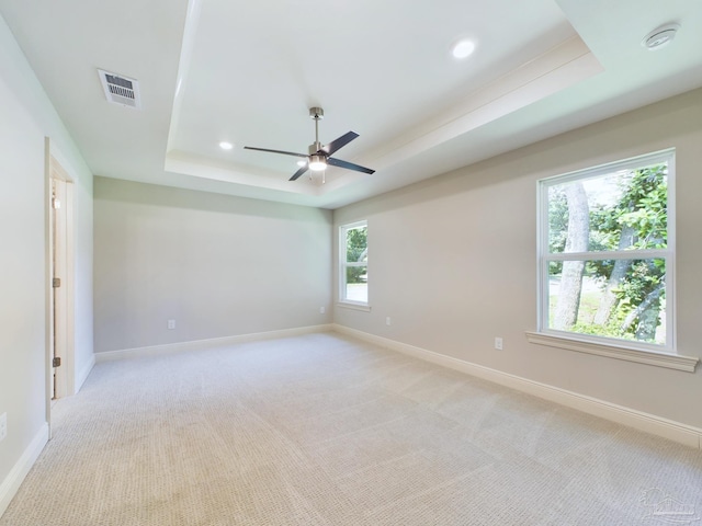 unfurnished room with a raised ceiling, visible vents, light carpet, and baseboards