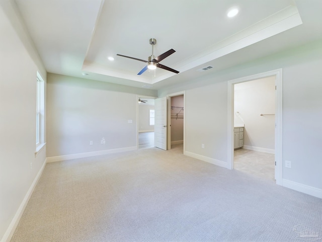 unfurnished bedroom featuring light colored carpet, a tray ceiling, visible vents, and baseboards