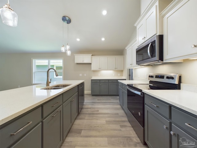 kitchen featuring pendant lighting, stainless steel appliances, a sink, and white cabinets