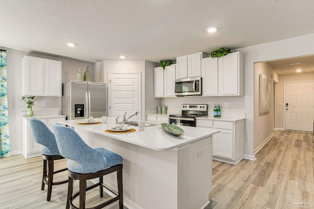 kitchen with sink, a textured ceiling, appliances with stainless steel finishes, an island with sink, and white cabinets