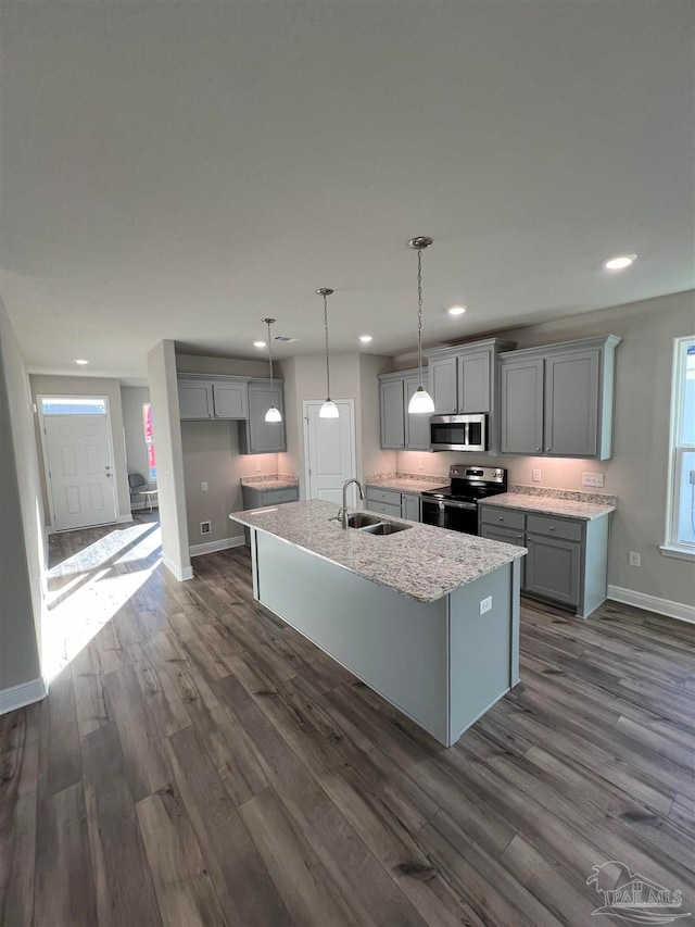 kitchen featuring sink, stainless steel appliances, decorative light fixtures, dark wood-type flooring, and a kitchen island with sink