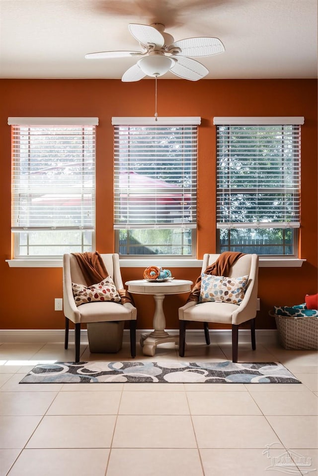 living area featuring light tile patterned floors, ceiling fan, and baseboards