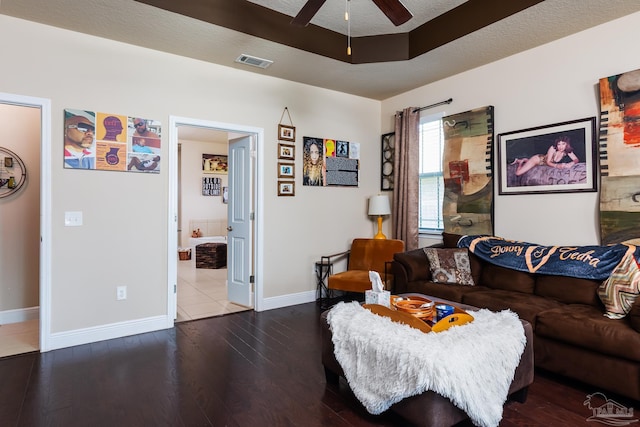 living area with a raised ceiling, visible vents, a ceiling fan, wood finished floors, and baseboards