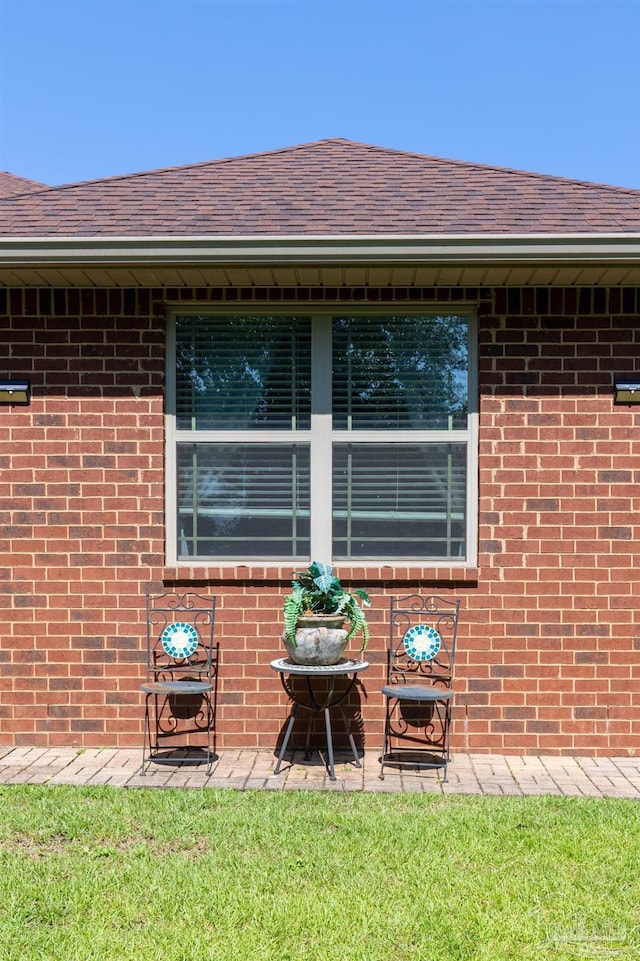 exterior space featuring roof with shingles, brick siding, a lawn, and a patio