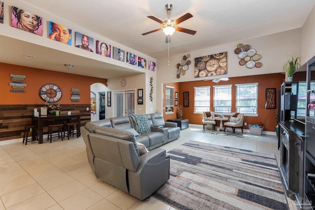 living area featuring arched walkways, ceiling fan, light tile patterned floors, and a textured ceiling