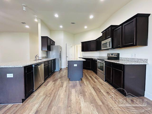 5643 Flume Dr, Pace, FL 32571 - kitchen featuring stainless steel appliances, light wood-type flooring, a center island, dark cabinets, and light stone counters