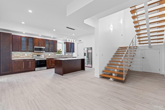 kitchen with hanging light fixtures, stainless steel appliances, backsplash, light hardwood / wood-style floors, and a kitchen island