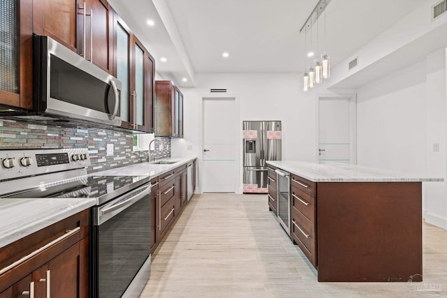 kitchen with pendant lighting, a center island, sink, light hardwood / wood-style flooring, and stainless steel appliances