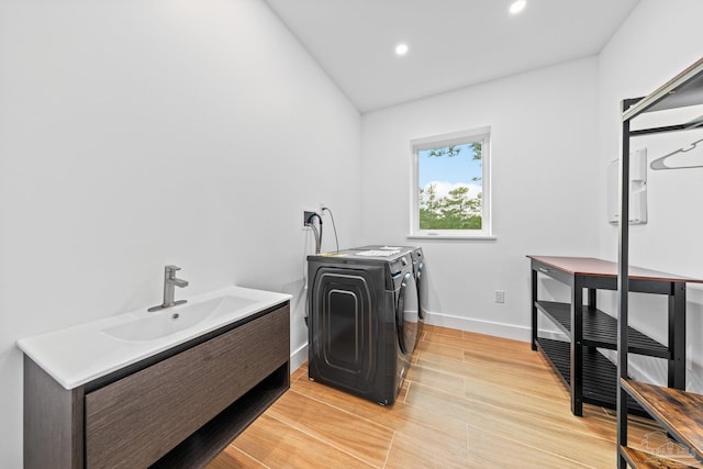 laundry area with washing machine and dryer, sink, and light hardwood / wood-style floors