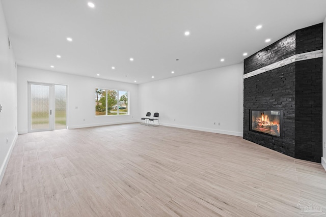 unfurnished living room featuring a stone fireplace and light wood-type flooring