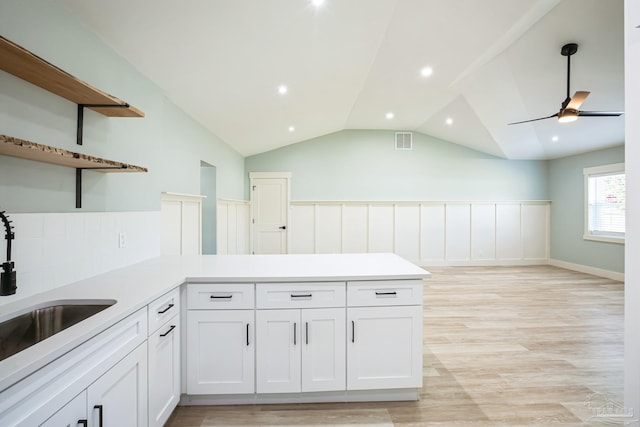 kitchen with lofted ceiling, white cabinets, sink, light hardwood / wood-style floors, and kitchen peninsula