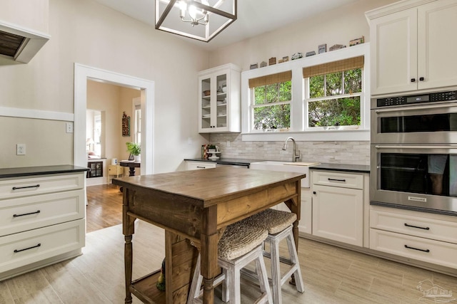 kitchen with dark countertops, stainless steel double oven, backsplash, and an inviting chandelier