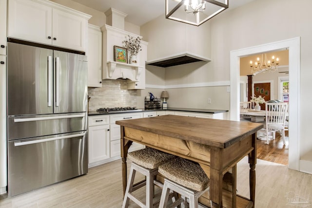 kitchen featuring tasteful backsplash, light wood-style flooring, appliances with stainless steel finishes, dark countertops, and an inviting chandelier