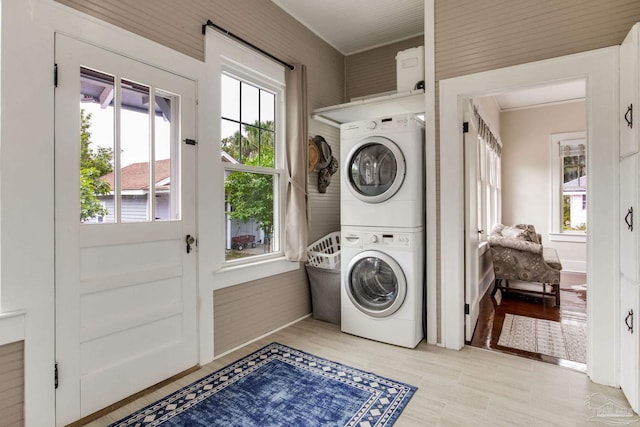 clothes washing area with stacked washer / dryer, light wood-style flooring, laundry area, and plenty of natural light