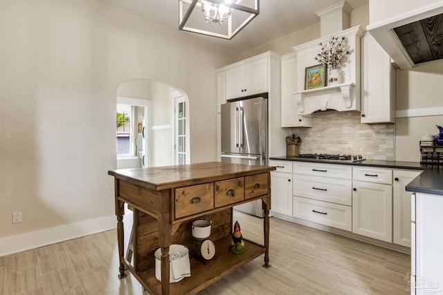 kitchen with arched walkways, decorative backsplash, appliances with stainless steel finishes, white cabinets, and dark countertops